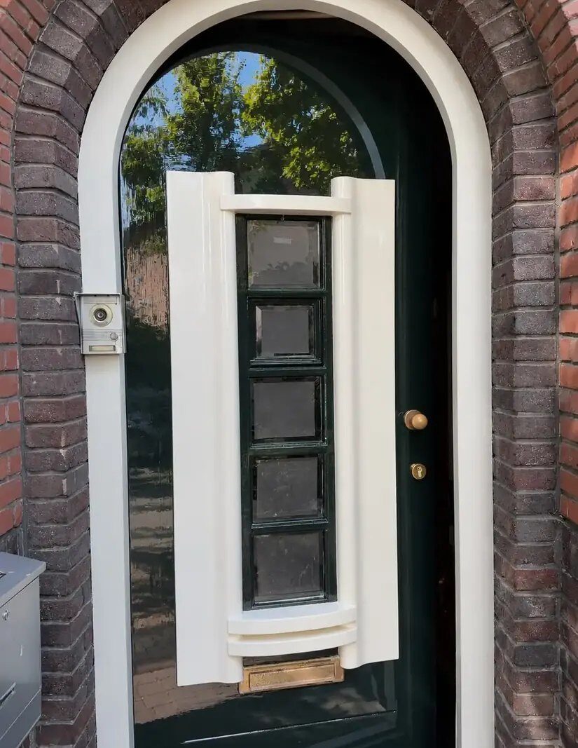 Boogvormige voordeur in donkergroen hoogglans met cremekleurige omlijsting en glas in lood