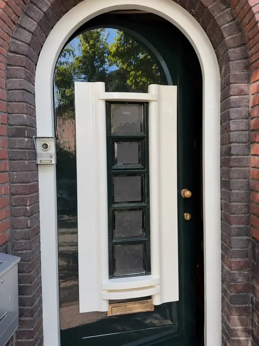 Boogvormige voordeur in donkergroen hoogglans met cremekleurige omlijsting en glas in lood